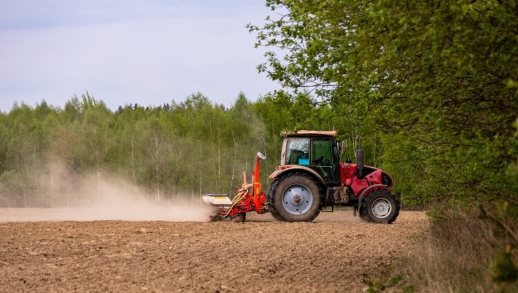 赤いトラクターが乾いた畑で土を巻き上げている光景