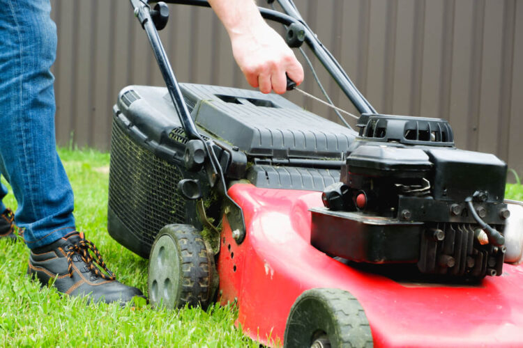 赤い草刈り機の側面とそれを操作しようとする人の手