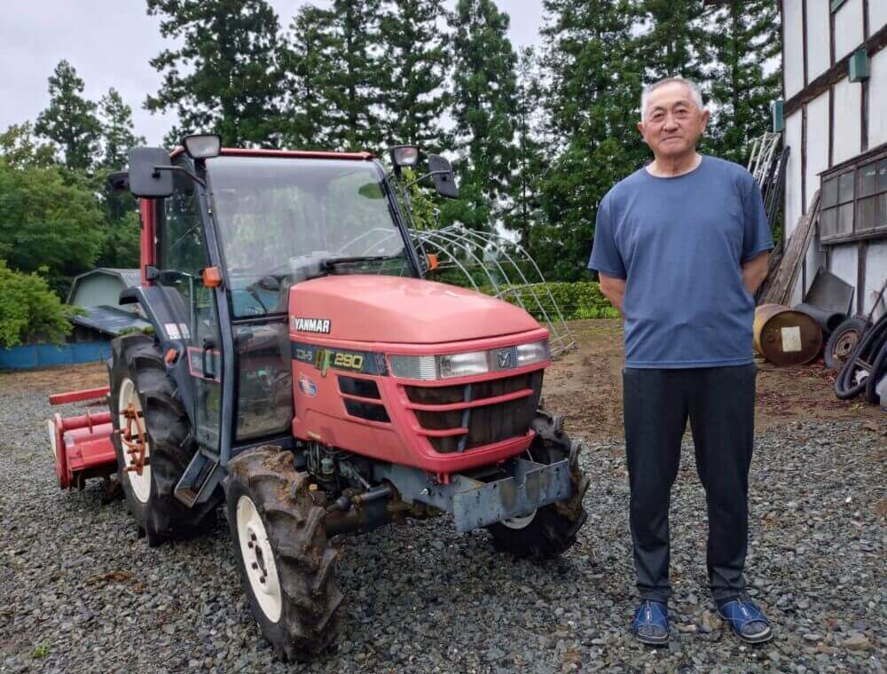 農家の男性と赤いトラクターが並んで写る写真